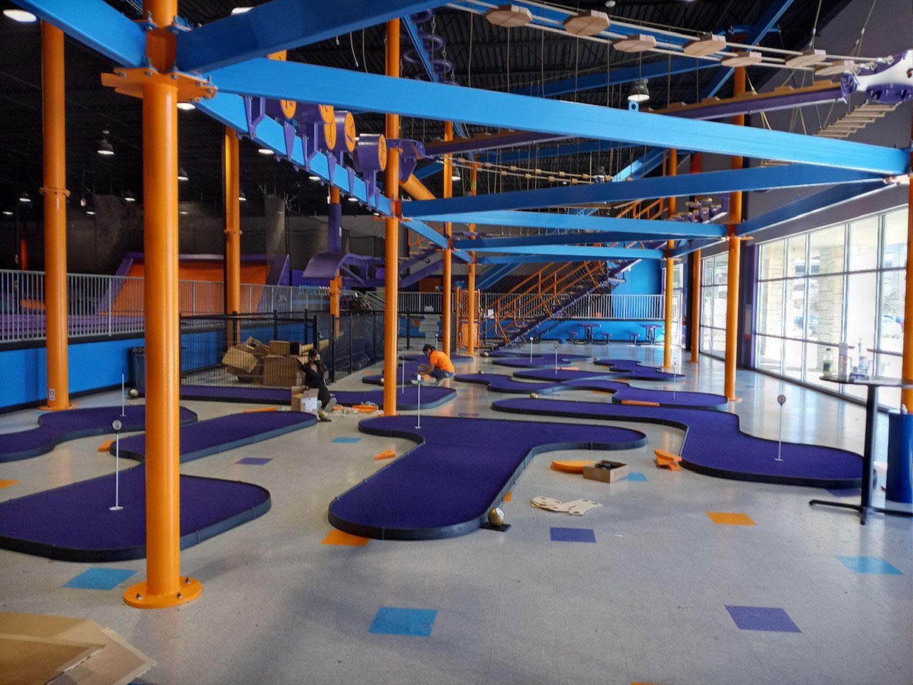 An Altitude Trampoline Park worker sorts orange obstacles to place on the purple turf of the MiniLinks miniature golf course