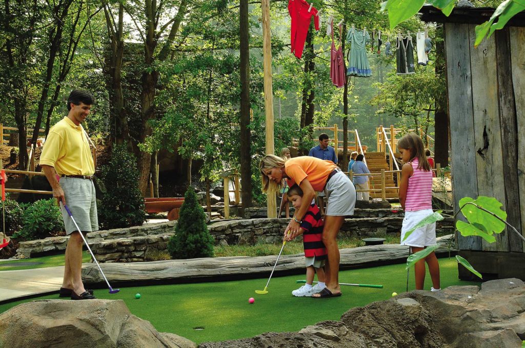 Mom helping son play mini golf on outdoor course in Gatlinburg