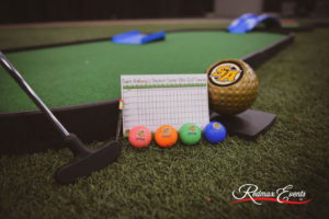 Variety of miniature golf accessories on display including a Soft Putter™, score cards, and golf balls in pink, orange, green, and blue respectively.