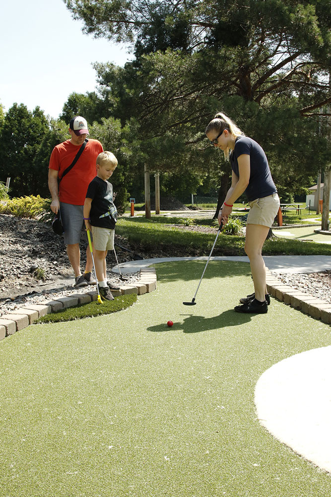 Dad and son watch mom putt on an AGS mini golf hole at Veterans Memorial Park in Richfield, MN