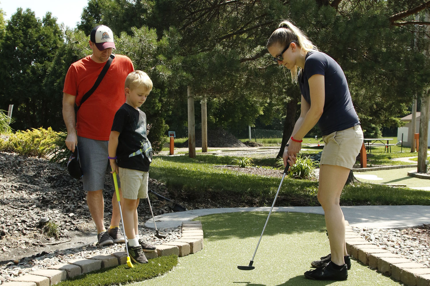 Dad and son watch mom putt on an AGS mini golf hole at Veterans Memorial Park in Richfield, MN