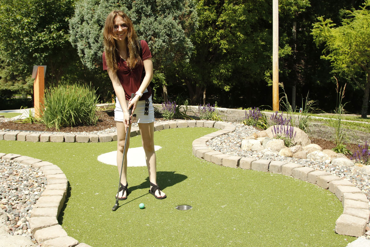 Smiling at the camera, a woman is positioned ready to shoot her mini golf ball into the hole at Veterans Memorial Park’s mini golf course installed by AGS.