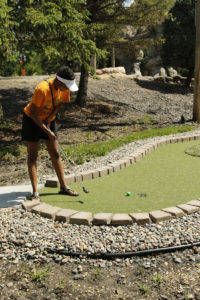 With her Soft Putter™ club swung forward and the mini golf ball moving toward the hole, a woman is pictured putting on one of the Modular Advantage® Mini Golf holes in Richfield, Minnesota.