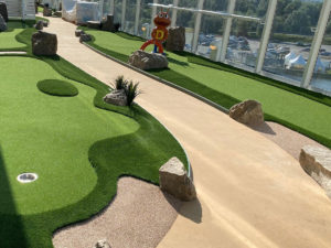 Miniature golf course greens along perimeter of AIDA Cosma cruise ship deck with walkway down the middle of the course.