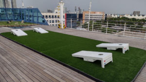 Stationed overlooking the buildings of Miami, bean bag toss set up on Oceania Insignia placed on rectangular Adventure Golf and Sports putting green.