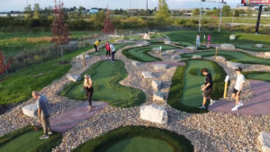 People playing on the Modular Advantage® mini golf course at Ryze Adventure Park. Rough turf, instead of paver bricks, define the hole shapes.