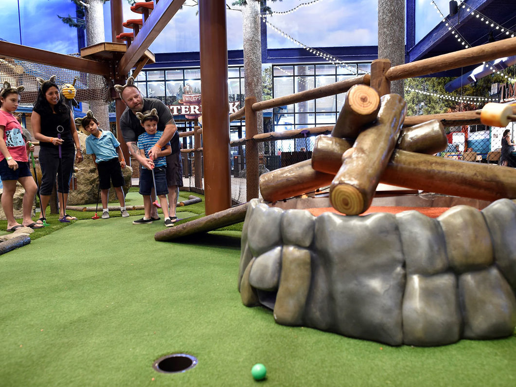 Family looks on as dad helps one of his sons putt a mini golf ball up a ramp at a Great Wolf Lodge