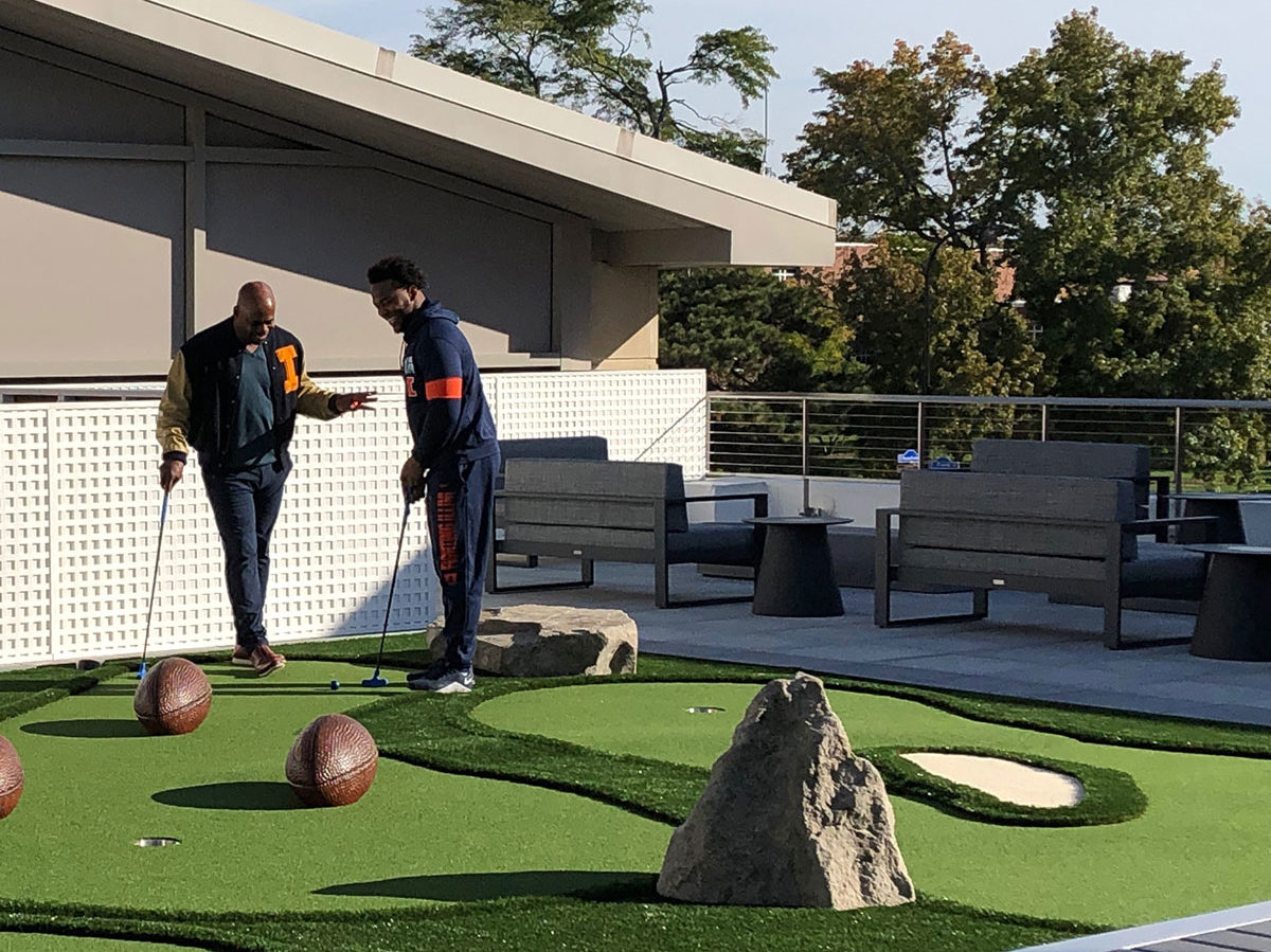 Two students share a laugh before putting around footballs on the U of I rooftop mini golf course