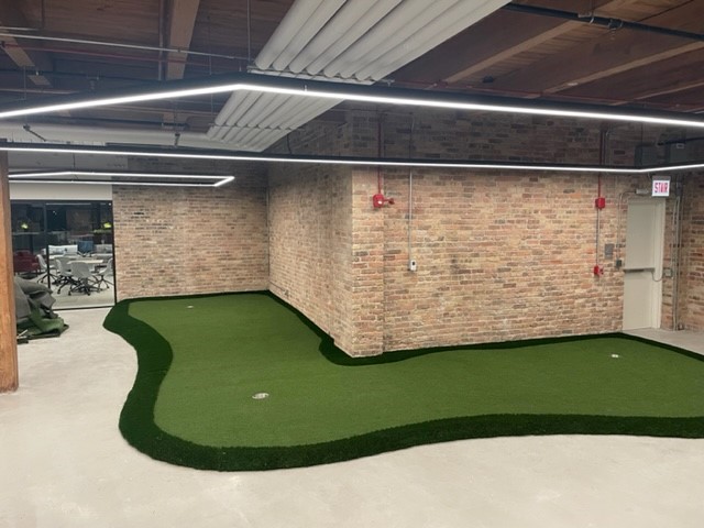 This three-hole custom modular putting green wraps around a brick corner wall at the Urban Innovations Office in a Chicago building