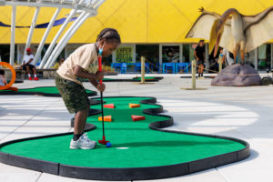 Young girl poised to make final putt on Jurassic miniature golf hole at the Brooklyn Children’s Museum
