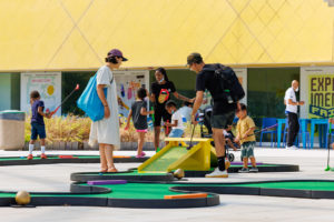 Parents watching young son’s putt to top of ramp obstacle on a hole at the Jurassic Mini-Golf course