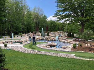 A young child is barely visible following a woman walking on one of the mini golf course greens