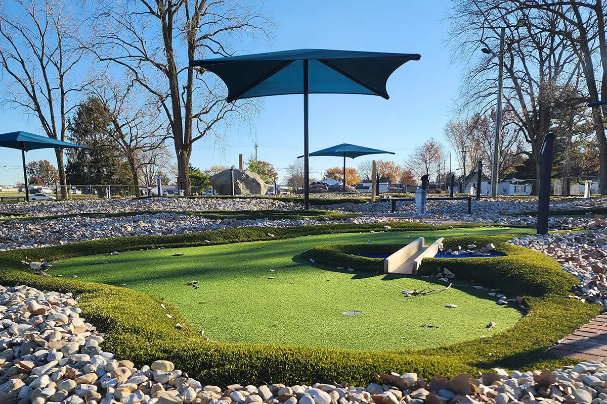 Mini Golf Course green at Cutler Park, Kokomo, IN, looks natural with sloping terrain and small wooden bridge amid rough turf